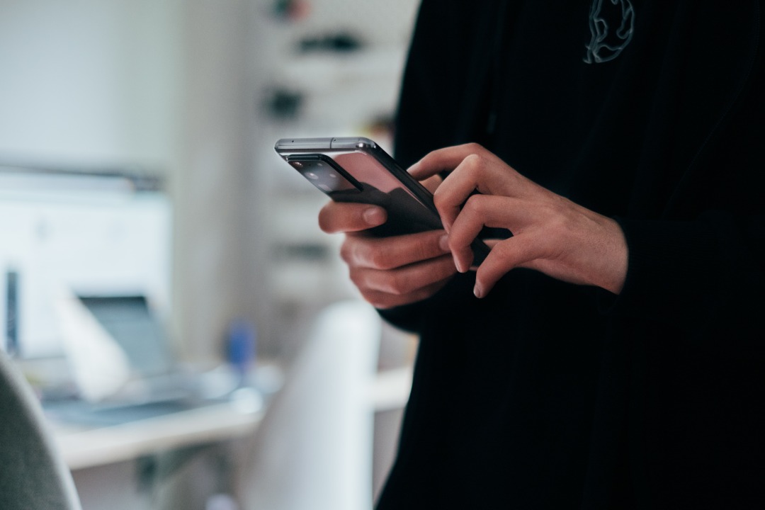 Young person holding a phone wearing a black jumper. Torso only.