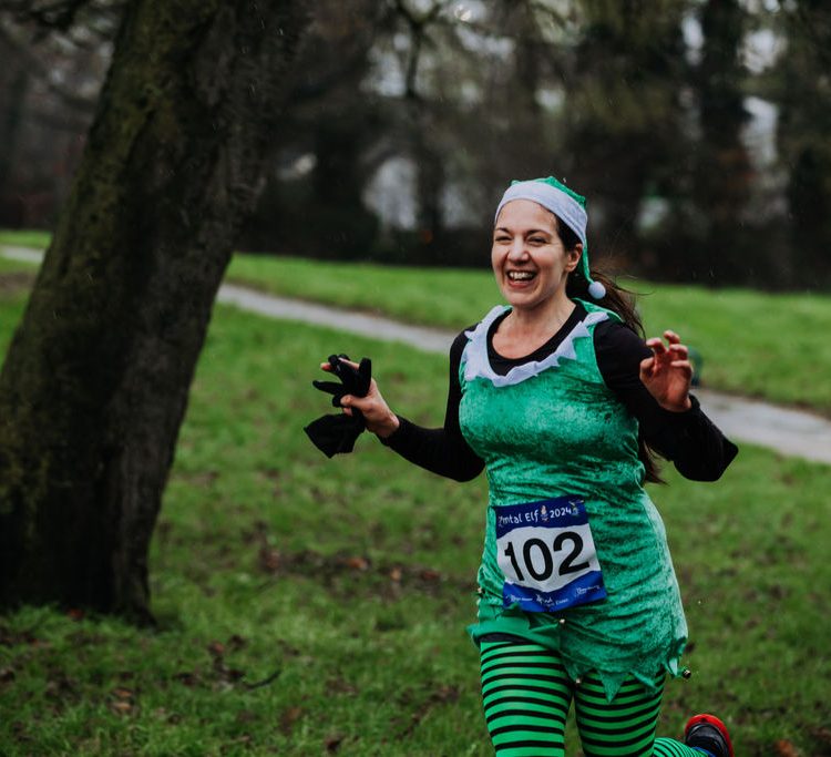 Runner in green outfit smiles with her hands out in front of her