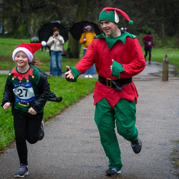 A man and a girl in Christmas outfits running towards the finish line