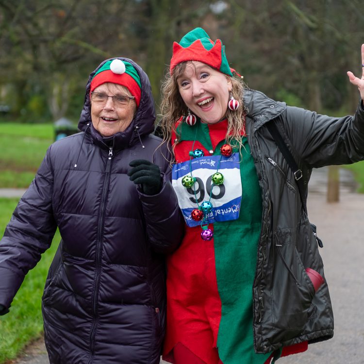 Two women in festive outfits walking along the course as one smiles and waves