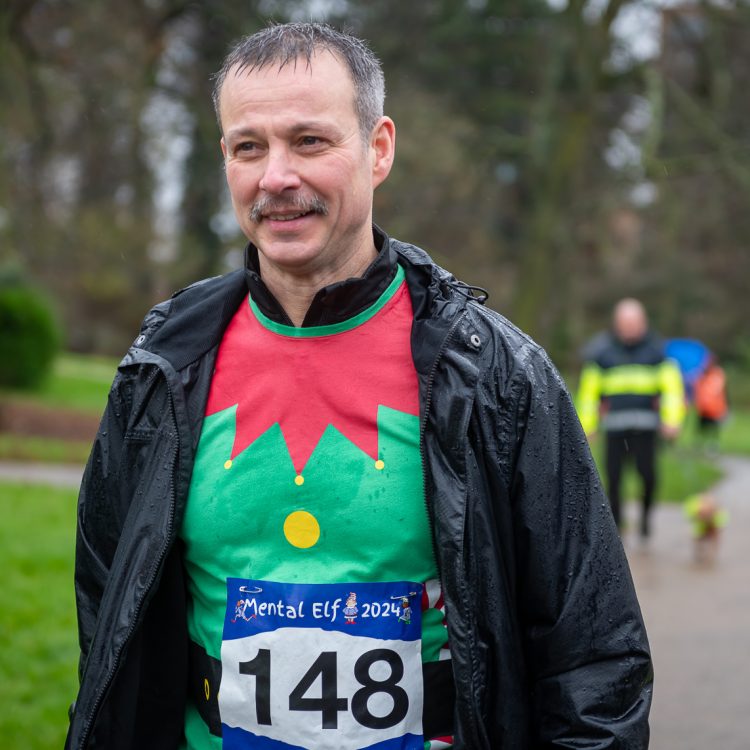 A runner wearing a black rain jacket over an elf t-shirt