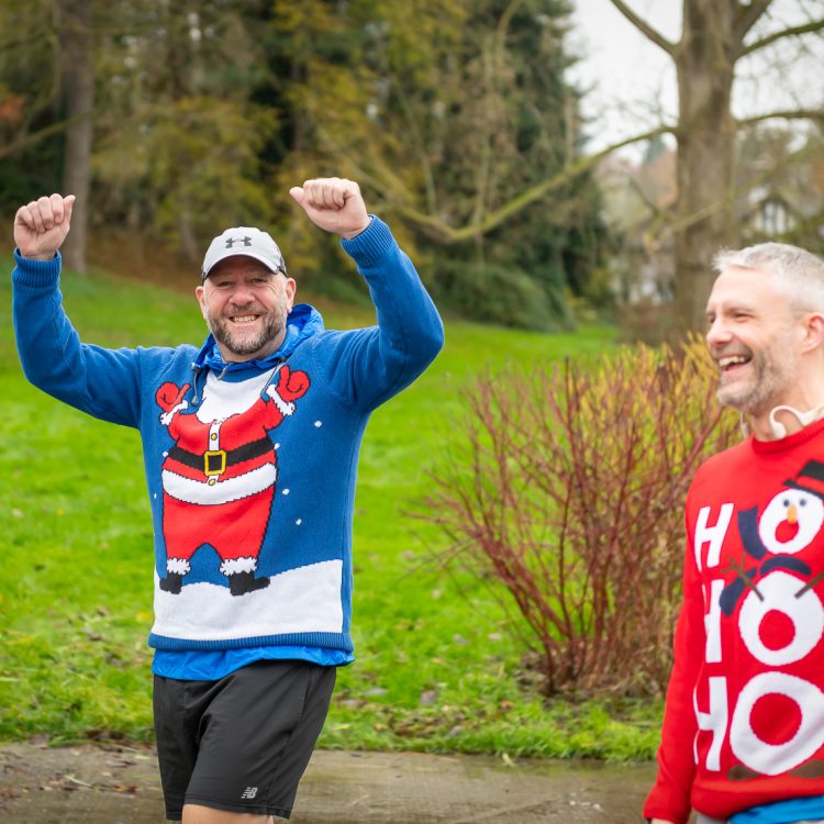Two smiling men wearing colourful Christmas jumpers