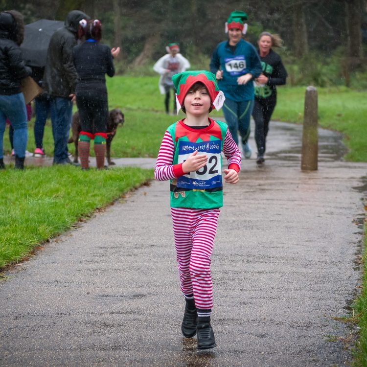 A young boy jogging in an elf outfit as other runners follow behind