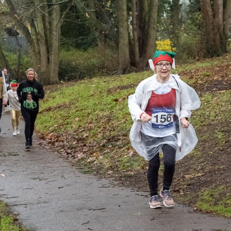 A woman wearing and elf hat and rain poncho jogging along the course