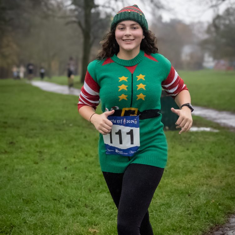 A young woman in an elf jumper and hat looks at the camera during the fun run