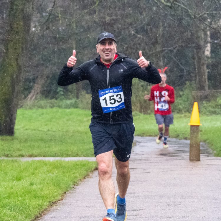 A man dressed in black smiling and giving thumbs up to the camera during the run