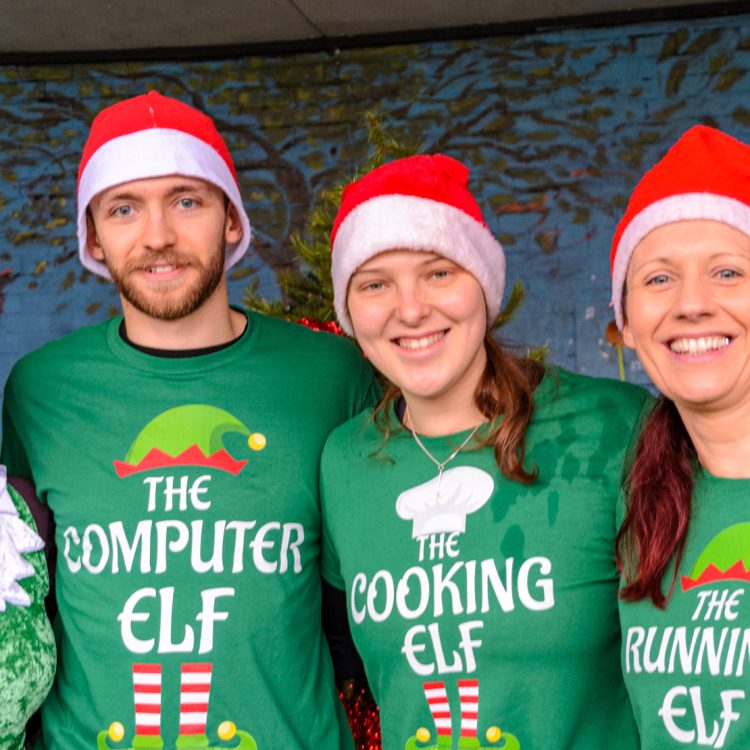 Four people in elf tops and Christmas hats smiling for the camera