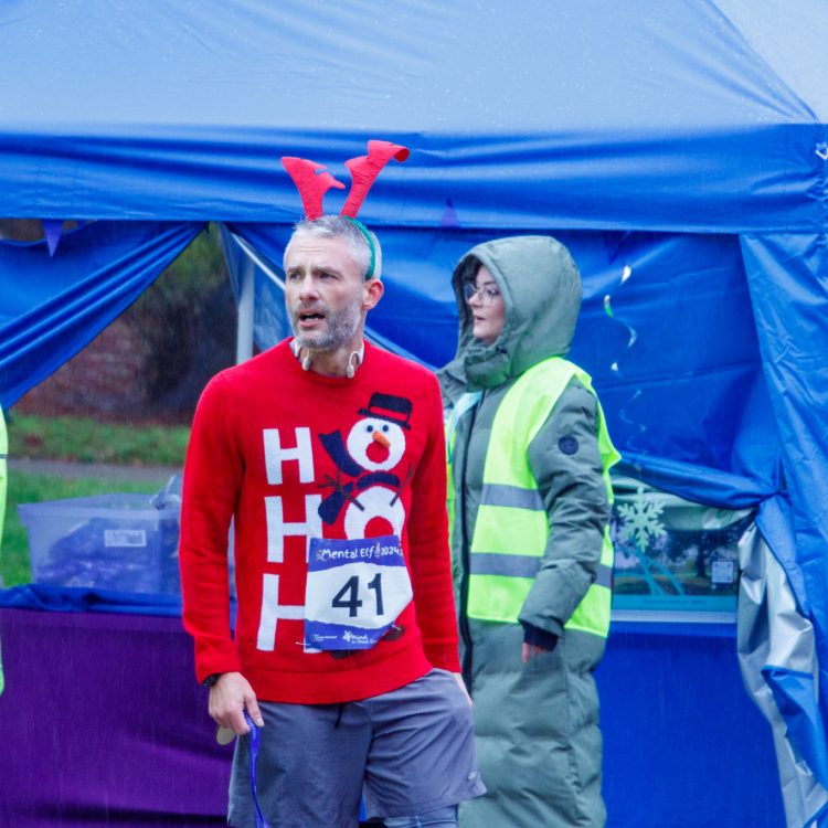 Man dressed in Christmas jumper and reindeer antlers.