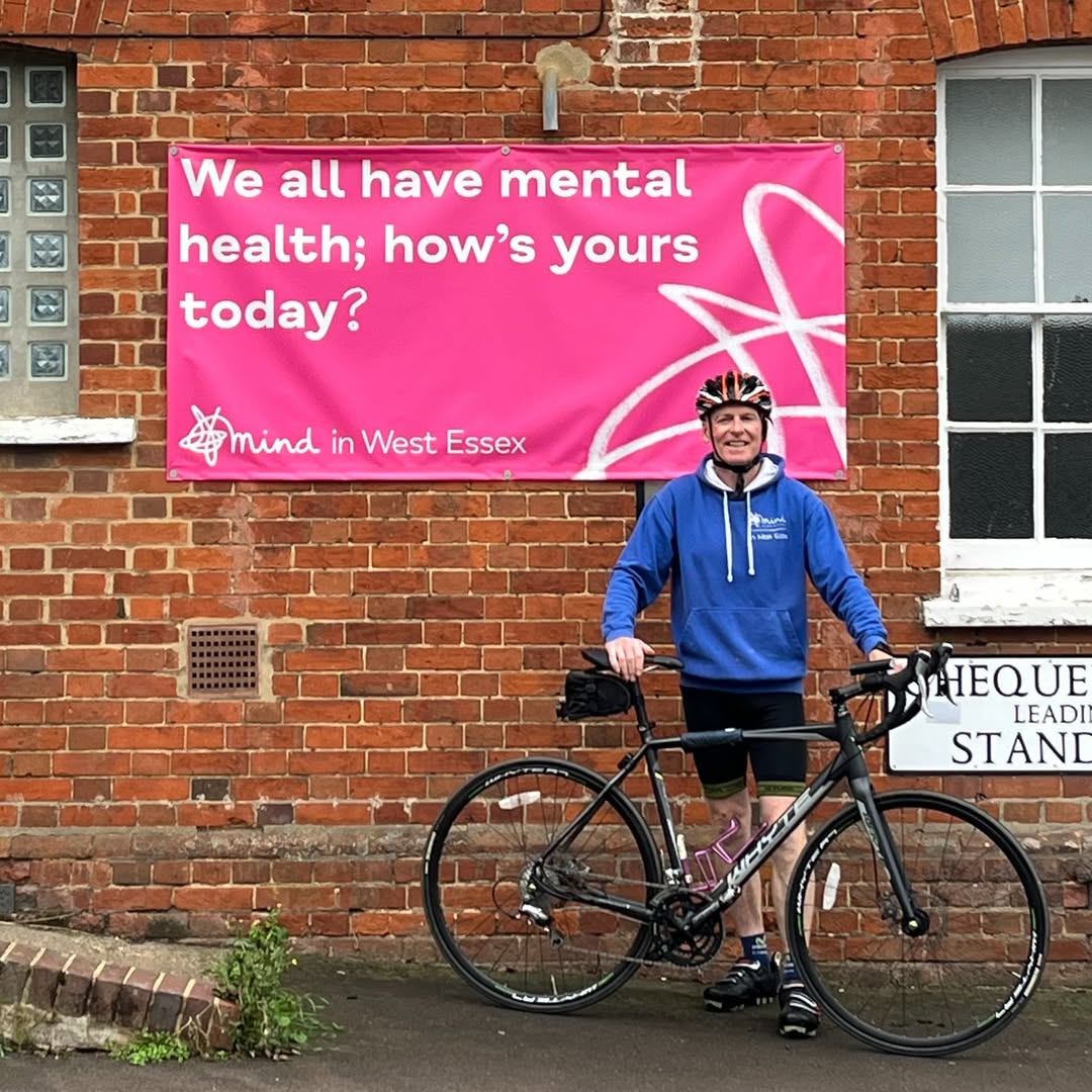 Man standing with bicycle next to a pink Mind in West Essex charity banner